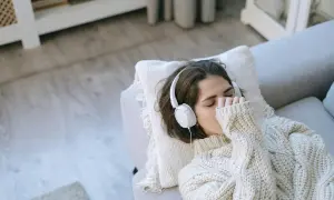 Junge Frau mit Kopfhörern auf dem Sofa, die Musik hört, um mit Depressionen umzugehen.