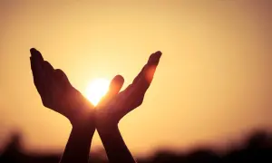Hände fangen die Sonne ein, ein Symbol dafür, was ist Hoffnung: Licht und Wärme in der Dunkelheit.