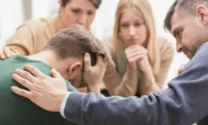 Unterstützung bei Depression: Eine Gruppe von Menschen tröstet einen Mann, der den Kopf in den Händen hält.