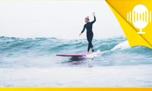 Surferin auf einer rosa Tafel, die mit erhobener Hand über die Wellen gleitet. Ein Symbol für das Lebensfreude wiederfinden.