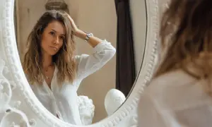 Frau im Spiegel, die sich die Haare richtet. Ein Hauch von **entitlement psychologie** in ihrem Blick, als würde sie sich selbst bewundern.