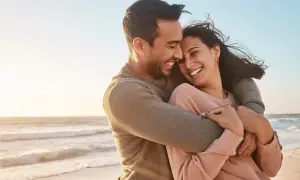 Glückliches Paar umarmt sich am Strand, lacht und genießt die Zeit. Ein perfekter Moment, um die Beziehung aufzufrischen.