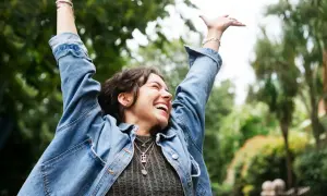Jubelnde Frau mit erhobenen Armen im Freien. Sie hat ihren Fokus trainieren und genießt den Moment.