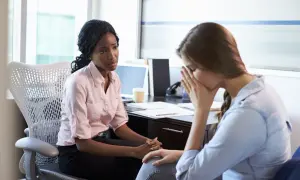 Zwei Frauen im Büro, eine spricht einfühlsam, die andere kämpft mit der Last der **Depression bei der Arbeit**.