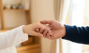 Zwei Hände halten sich fest, ein Ring am Finger. Die Nähe ist tröstlich, doch die Angst vor einer Fernbeziehung schwingt mit.