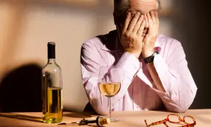 Mann mit Händen vor dem Gesicht, Wein, Korkenzieher und Brille auf dem Tisch. Ein Bild, das die Verzweiflung und die Folgen von Korsakow-Syndrom symbolisiert.