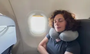 Frau schläft entspannt im Flugzeug mit Nackenkissen. Ein Beweis, warum man keine Angst vorm Fliegen haben muss.