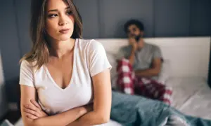 Eine Frau blickt nachdenklich weg, während ein Mann im Hintergrund sitzt. Die Stimmung ist angespannt, ein Zeichen, wann ist eine beziehung nicht mehr zu retten.