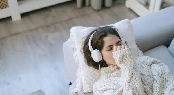 Junge Frau mit Kopfhörern auf dem Sofa, die Musik hört, um mit Depressionen umzugehen.