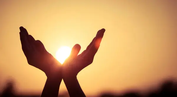Hände fangen die Sonne ein, ein Symbol dafür, was ist Hoffnung: Licht und Wärme in der Dunkelheit.