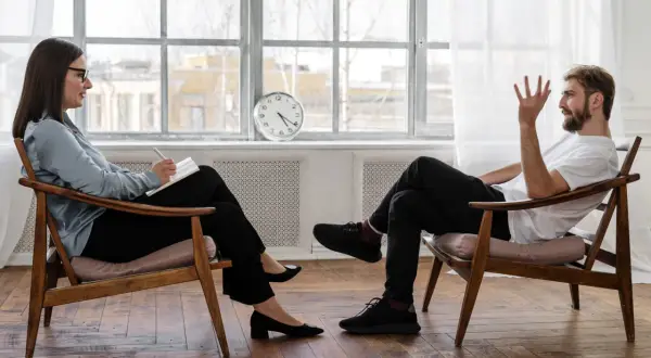 Frau in psychotherapie klinik macht Notizen, während Mann spricht.