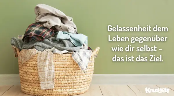 Ein Wäschekorb voller Kleidung vor einer grünen Wand. Der Spruch "Gelassenheit dem Leben gegenüber wie dir selbst – das ist das Ziel" lädt dazu ein, das eigene Bewusstsein zu erweitern.