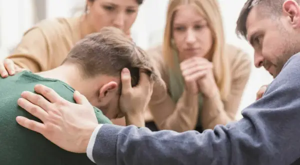 Unterstützung bei Depression: Eine Gruppe von Menschen tröstet einen Mann, der den Kopf in den Händen hält.