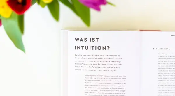 Blumen und ein Buch über Intuition. Lerne, deine Intuition zu trainieren und dem Bauchgefühl zu vertrauen.