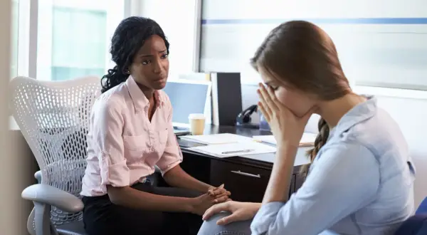 Zwei Frauen im Büro, eine spricht einfühlsam, die andere kämpft mit der Last der **Depression bei der Arbeit**.