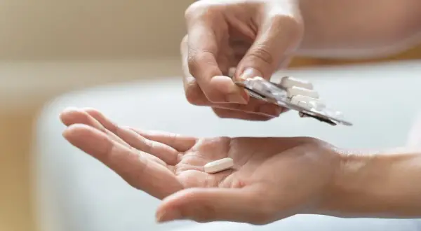 Eine Hand hält eine Tablette aus einer Blisterpackung, während eine andere Hand eine einzelne Tablette auffängt. Mögliche pregabalin nebenwirkungen im Blick.