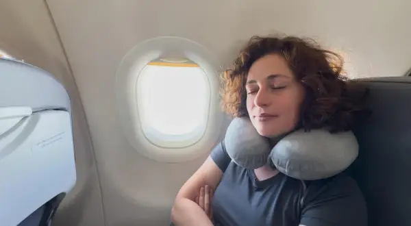 Frau schläft entspannt im Flugzeug mit Nackenkissen. Ein Beweis, warum man keine Angst vorm Fliegen haben muss.