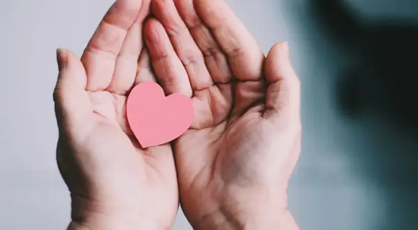 Zwei Hände halten ein rosa Herz. Ein Symbol für Geben und Nehmen, Liebe und Fürsorge.