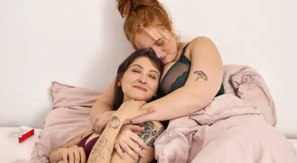 Zwei Frauen kuscheln im Bett. Ihre Nähe und Zärtlichkeit zeigen die wahre Bedeutung von Sexappeal: tiefe Verbundenheit und Intimität.
