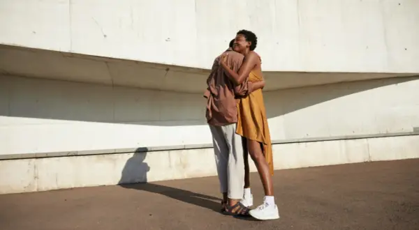 Ein Paar umarmt sich innig vor einer Betonwand. Ihre Körperhaltung strahlt tiefe **liebe und vertrauen** aus, ein Moment der Verbundenheit im hellen Sonnenlicht.