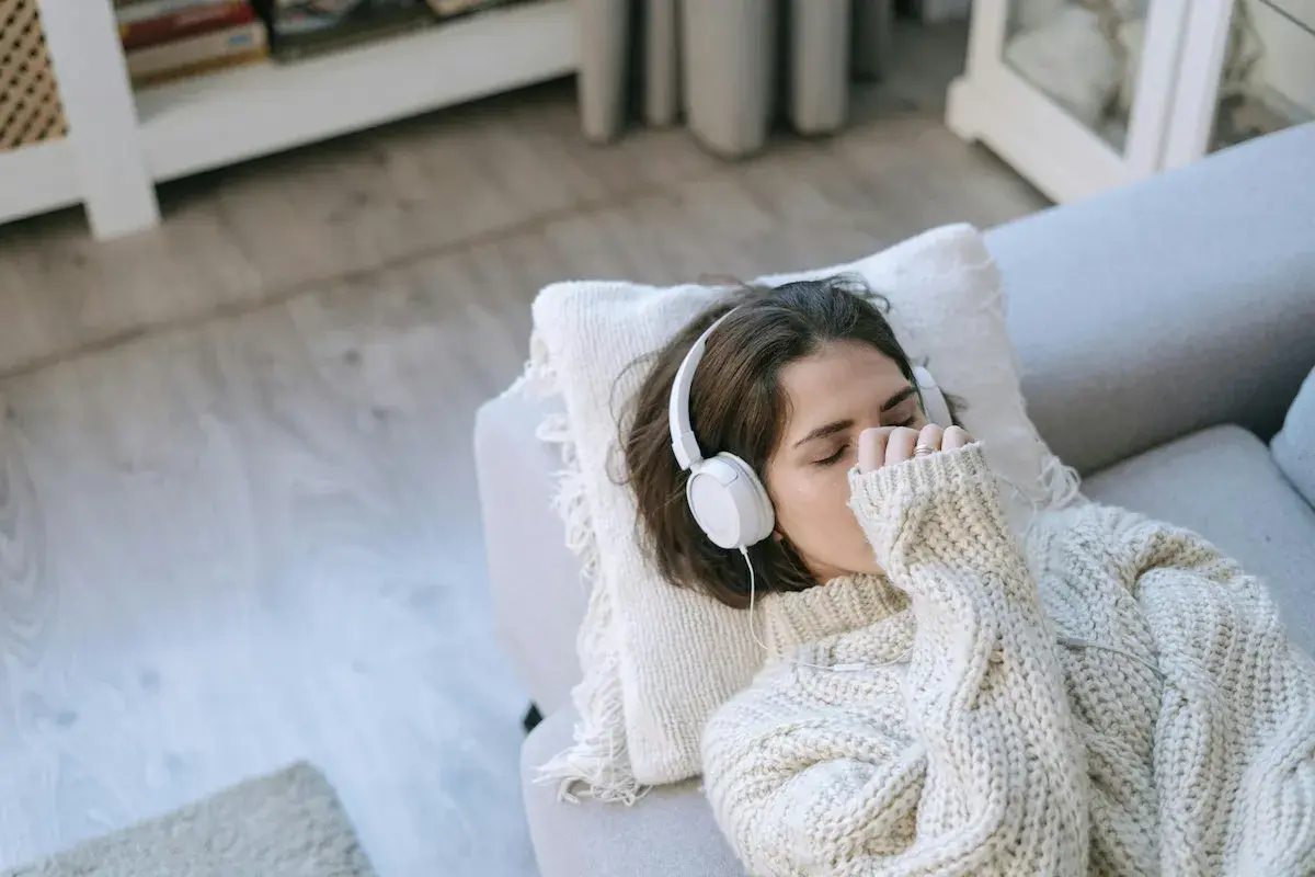 Junge Frau mit Kopfhörern auf dem Sofa, die Musik hört, um mit Depressionen umzugehen.