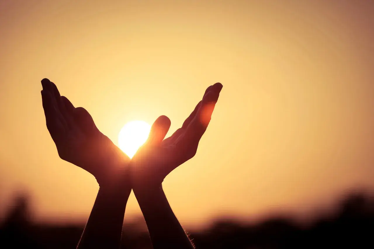 Hände fangen die Sonne ein, ein Symbol dafür, was ist Hoffnung: Licht und Wärme in der Dunkelheit.