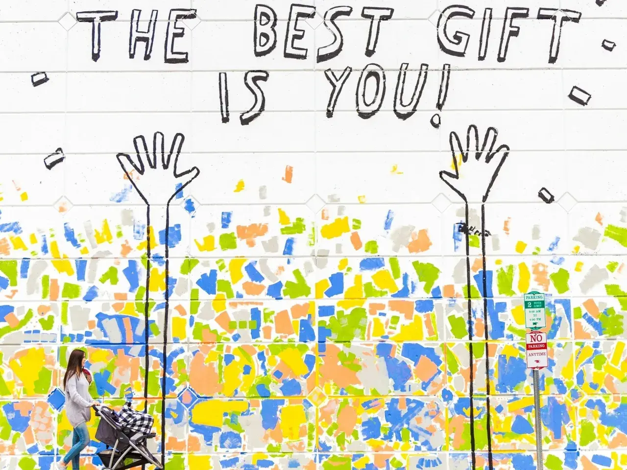 Bunte Wandmalerei mit der Botschaft "The best gift is you!". Eine Frau schiebt einen Kinderwagen. Dies erinnert an die psychologischen werte tests, die uns lehren, uns selbst wertzuschätzen.
