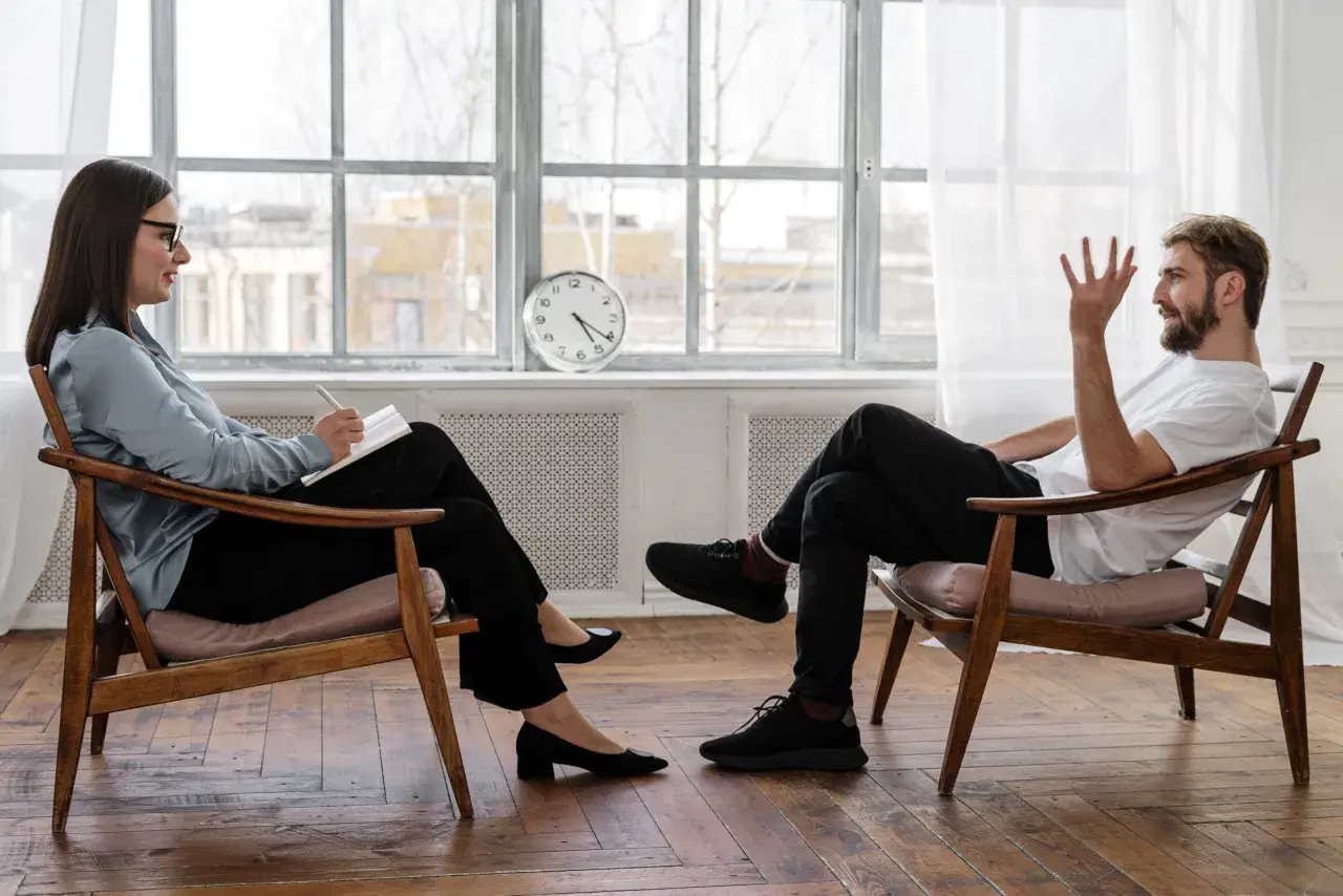 Frau in psychotherapie klinik macht Notizen, während Mann spricht.