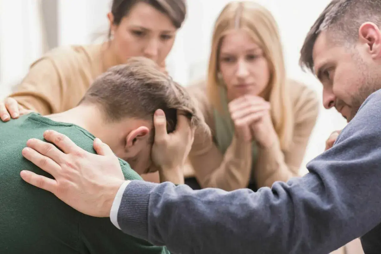 Unterstützung bei Depression: Eine Gruppe von Menschen tröstet einen Mann, der den Kopf in den Händen hält.