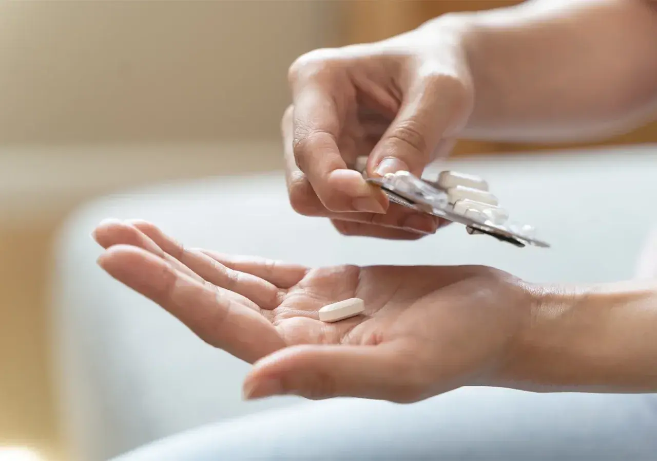 Eine Hand hält eine Tablette aus einer Blisterpackung, während eine andere Hand eine einzelne Tablette auffängt. Mögliche pregabalin nebenwirkungen im Blick.