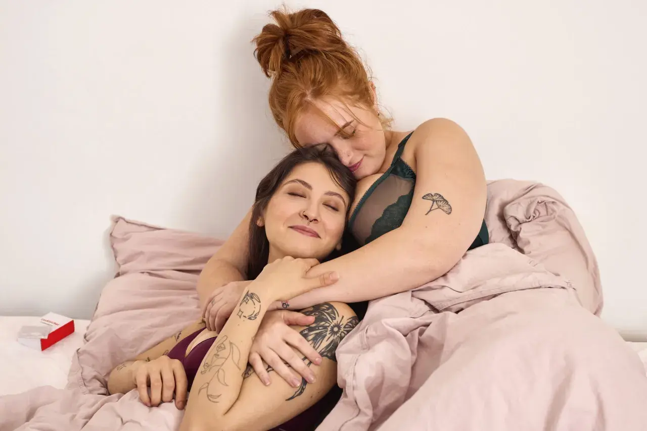 Zwei Frauen kuscheln im Bett. Ihre Nähe und Zärtlichkeit zeigen die wahre Bedeutung von Sexappeal: tiefe Verbundenheit und Intimität.