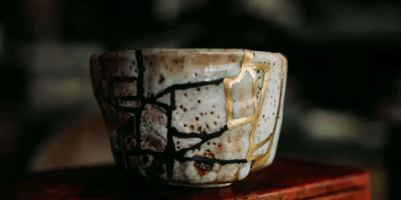 Zerbrochene Keramik, repariert mit Gold, symbolisiert die Kintsugi Psychologie: Narben machen uns stärker und schöner.