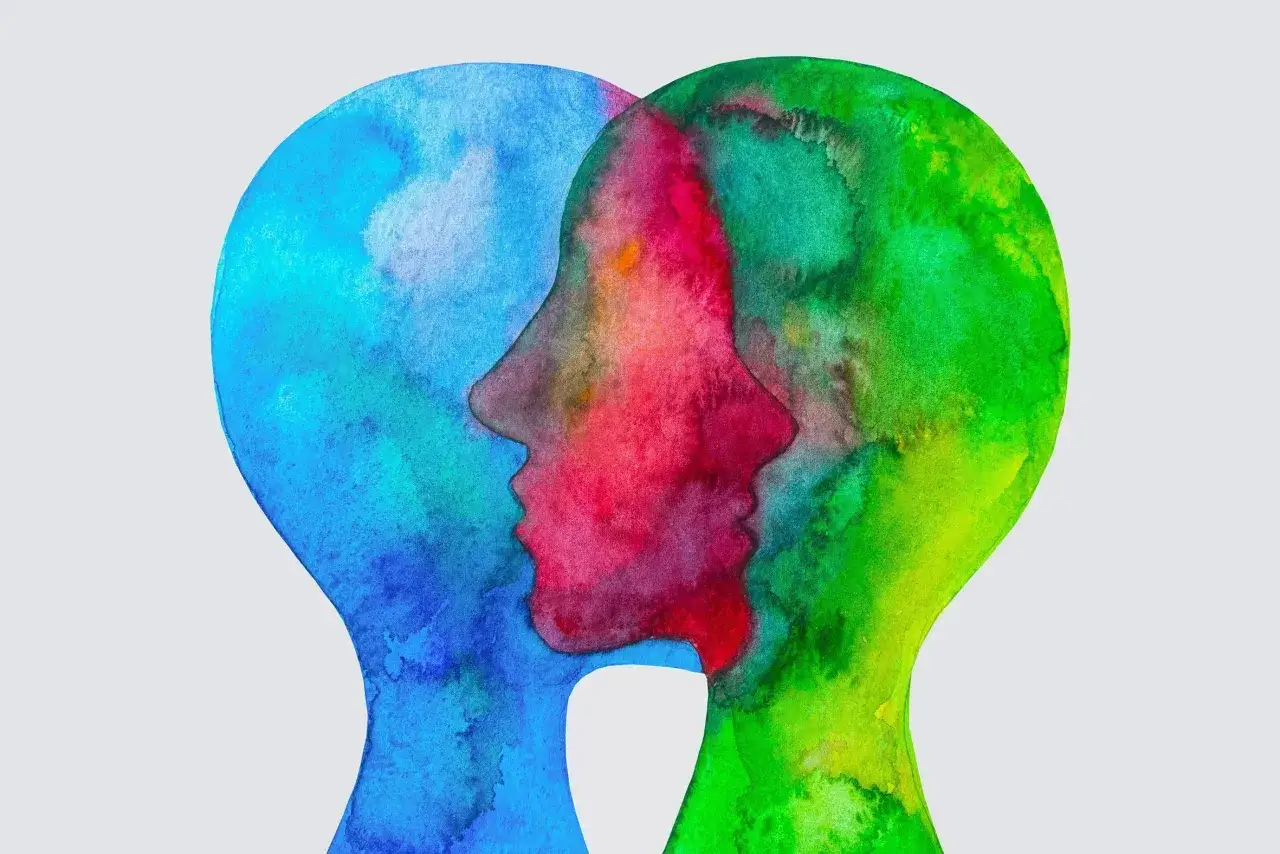Zwei stilisierte Köpfe in Aquarell, die sich überlappen. Ein blauer Kopf, ein roter und ein grüner. Ein empathieloser Mensch kann sich nicht in andere hineinversetzen.