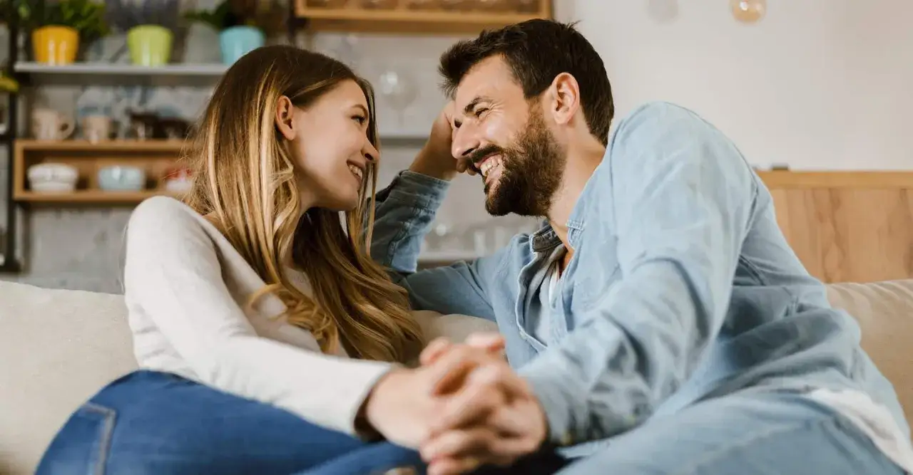 Ein Paar sitzt eng beieinander, h&auml;lt H&auml;ndchen und lacht sich an. Ihre Blicke voller Liebe und Vertrauen erz&auml;hlen eine stille Geschichte.