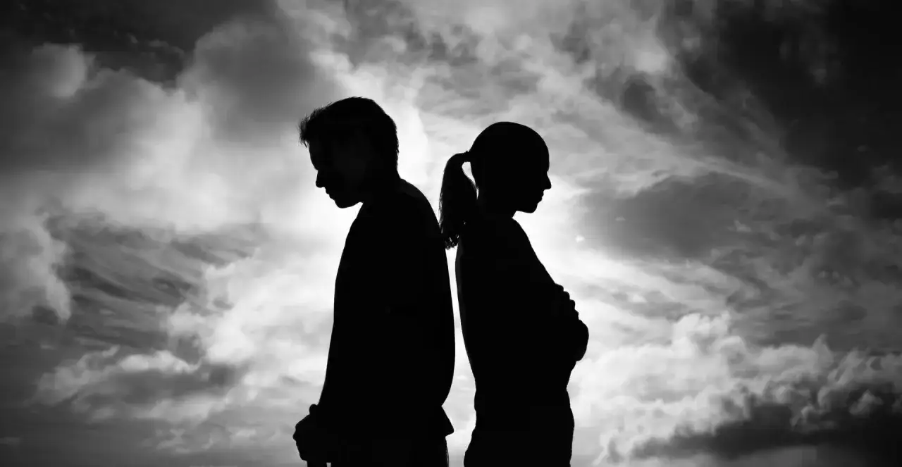 Silhouetten eines Paares, Rücken an Rücken, vor dramatischem Himmel. Ihre Körperhaltung drückt Entfremdung aus, ein Gefühl von Angst und verlorener Liebe.