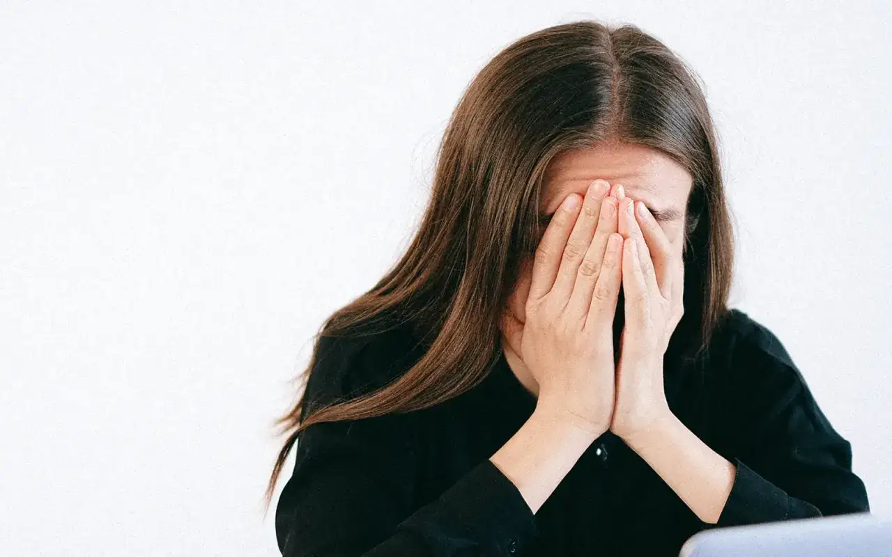 Eine Frau mit langen braunen Haaren bedeckt ihr Gesicht mit den H&auml;nden, als w&uuml;rde sie grundlos weinen.