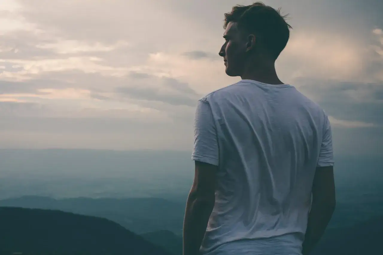 Ein Mann im wei&szlig;en T-Shirt blickt in die Ferne &uuml;ber eine neblige Landschaft. Er f&uuml;hlt sich klein, ich bin nicht wichtig.