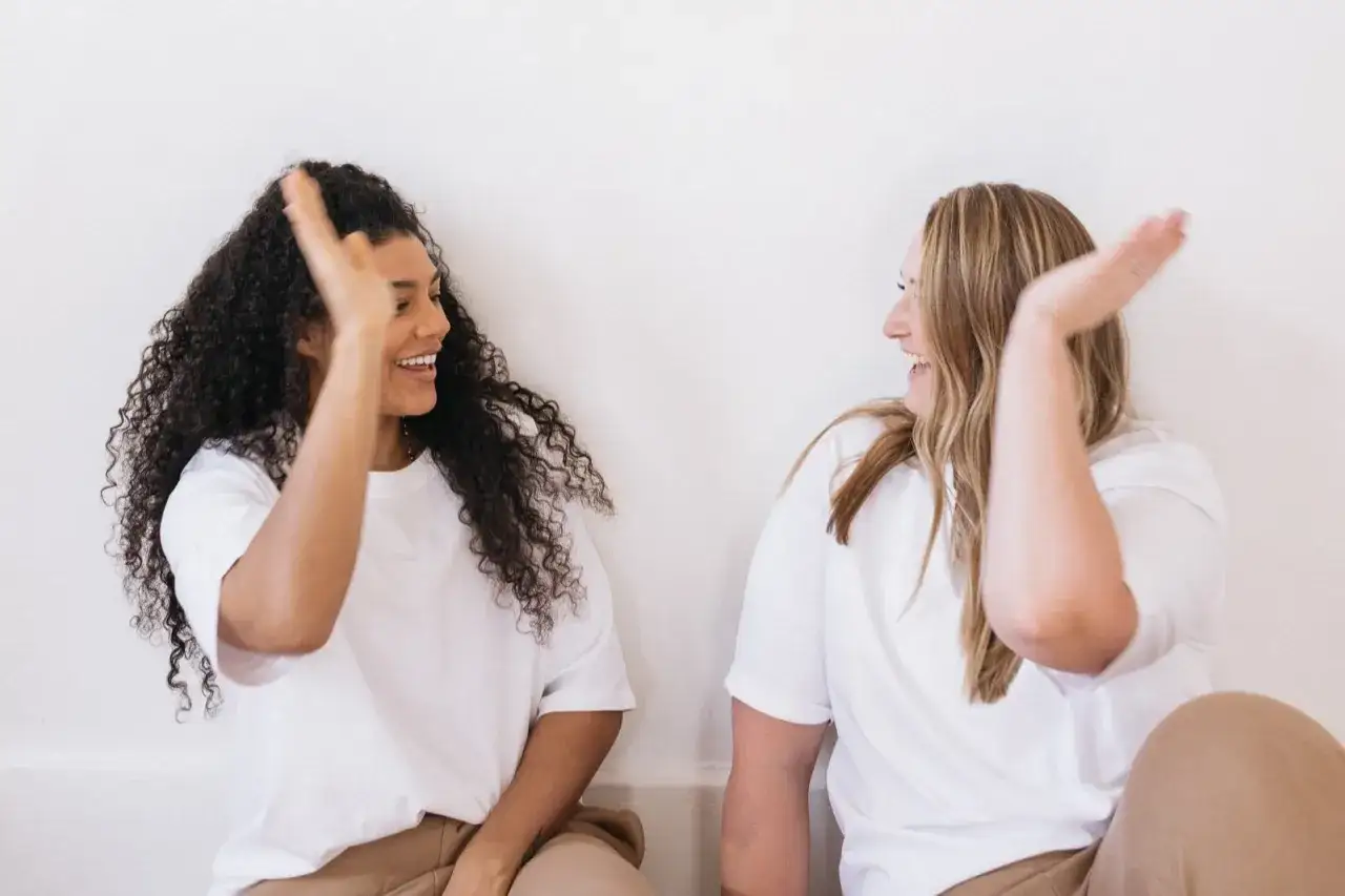 Zwei lachende Frauen geben sich High Fives. Ein Bild, das zeigt, wie man die Opferrolle Psychologie überwindet und positive Verbindungen schafft.