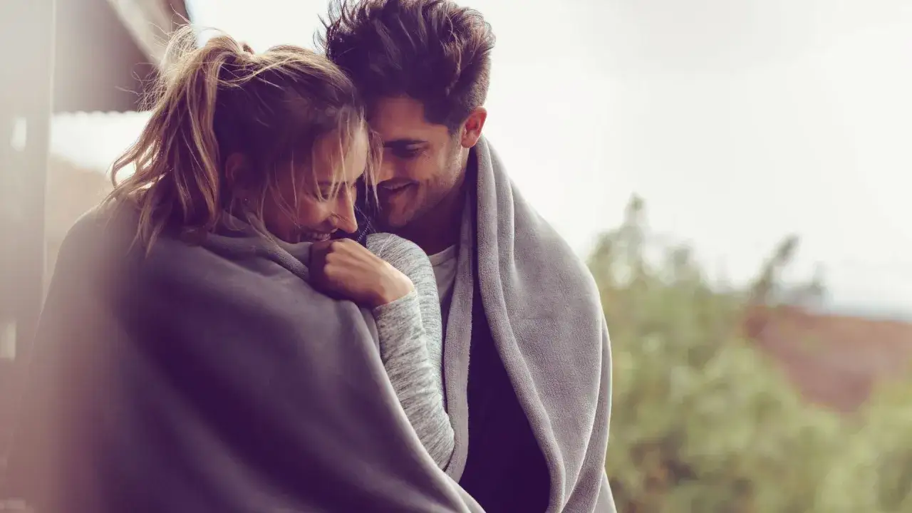 Ein Mann und eine Frau kuscheln sich in eine Decke. Sie lachen und schauen sich an. Es ist, als ob ein Mann Angst vor einer Frau hat, aber sie ist so lieb, dass er sich entspannt.