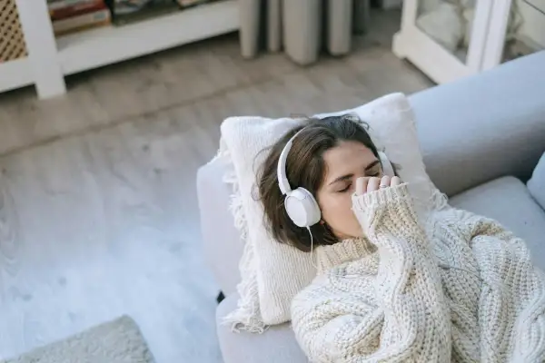 Junge Frau mit Kopfhörern auf dem Sofa, die Musik hört, um mit Depressionen umzugehen.
