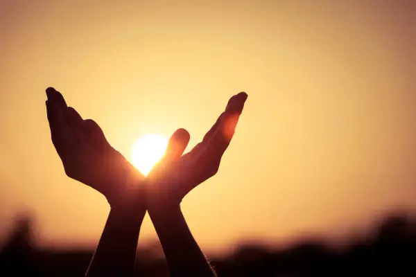 Hände fangen die Sonne ein, ein Symbol dafür, was ist Hoffnung: Licht und Wärme in der Dunkelheit.