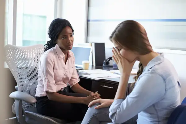 Zwei Frauen im Büro, eine spricht einfühlsam, die andere kämpft mit der Last der **Depression bei der Arbeit**.