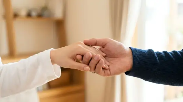 Zwei Hände halten sich fest, ein Ring am Finger. Die Nähe ist tröstlich, doch die Angst vor einer Fernbeziehung schwingt mit.