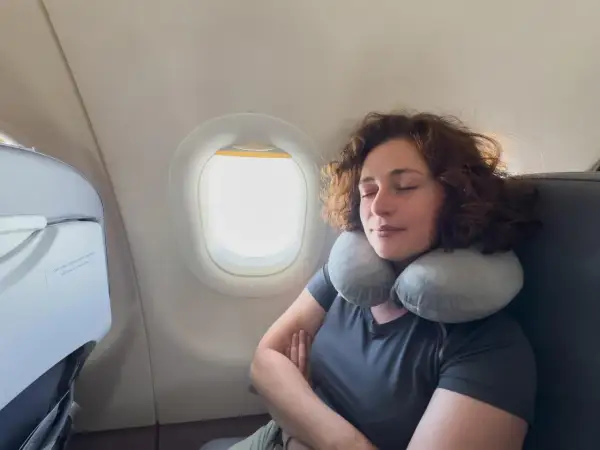 Frau schläft entspannt im Flugzeug mit Nackenkissen. Ein Beweis, warum man keine Angst vorm Fliegen haben muss.