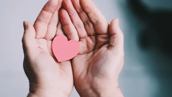 Zwei Hände halten ein rosa Herz. Ein Symbol für Geben und Nehmen, Liebe und Fürsorge.