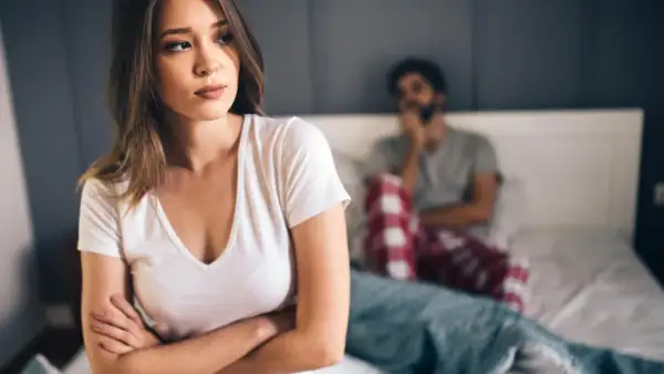 Eine Frau blickt nachdenklich weg, während ein Mann im Hintergrund sitzt. Die Stimmung ist angespannt, ein Zeichen, wann ist eine beziehung nicht mehr zu retten.